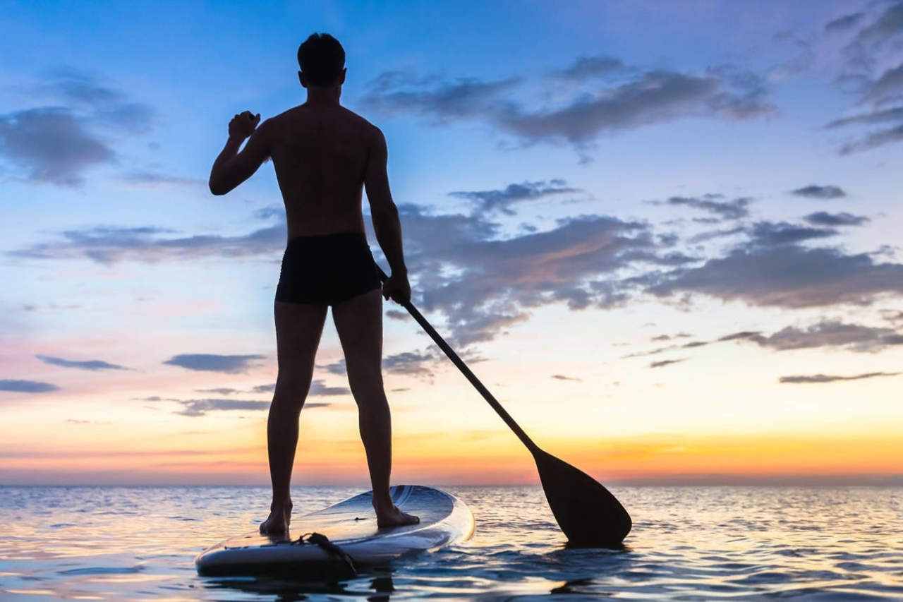 Sup al tramonto sul mare con uomo sportivo